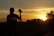 Smiling traveler holding a camera with a vibrant sunset backdrop on a safari trip.