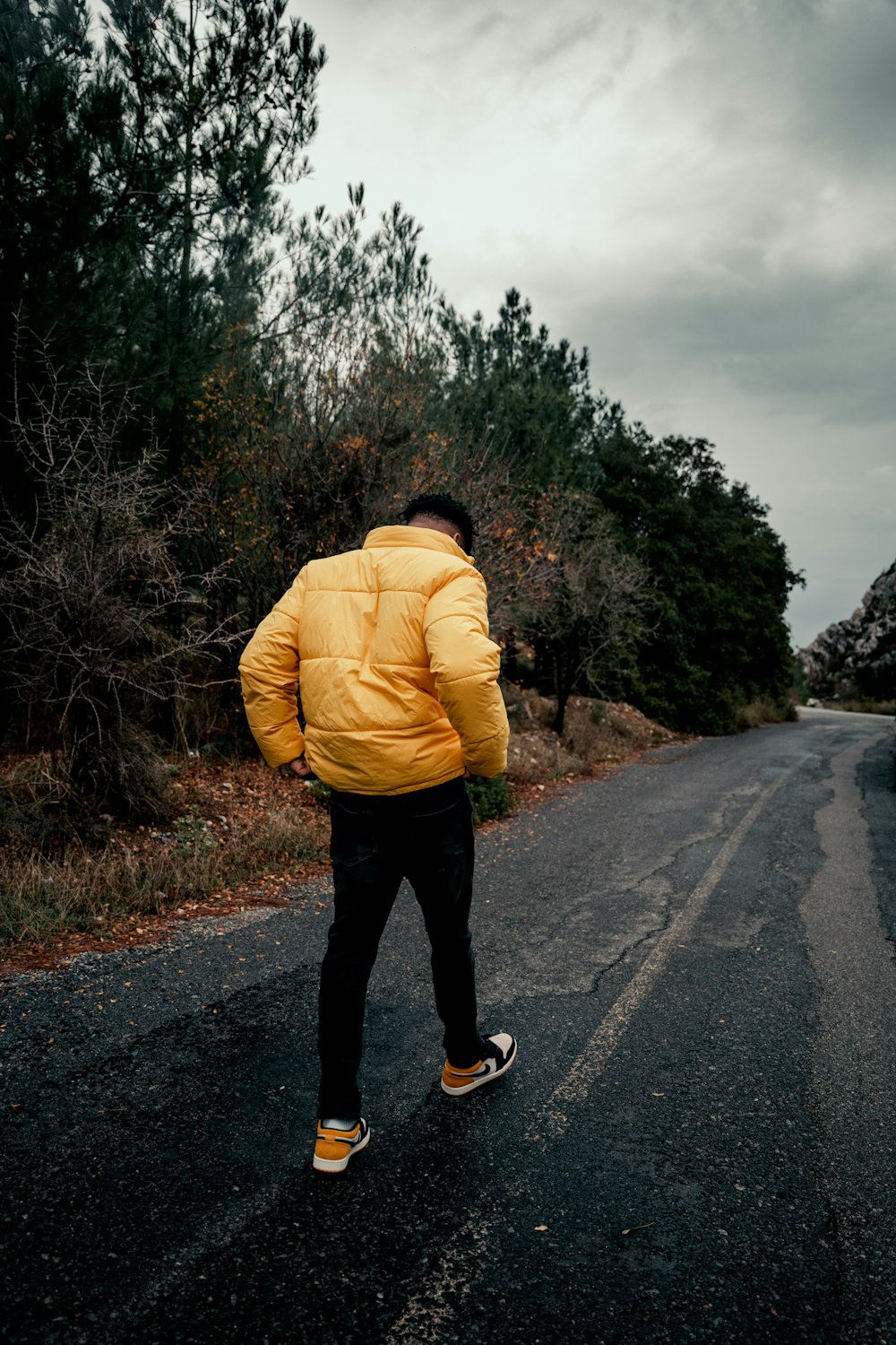 man in yellow jacket and black pants standing on road during daytime
