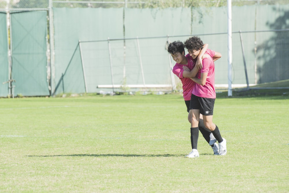 woman in pink shirt and black shorts running on green grass field during daytime