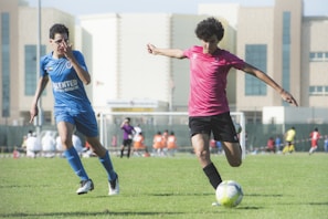 man in red shirt and black shorts playing soccer during daytime