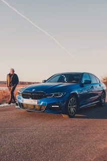 man in black jacket standing beside blue bmw car
