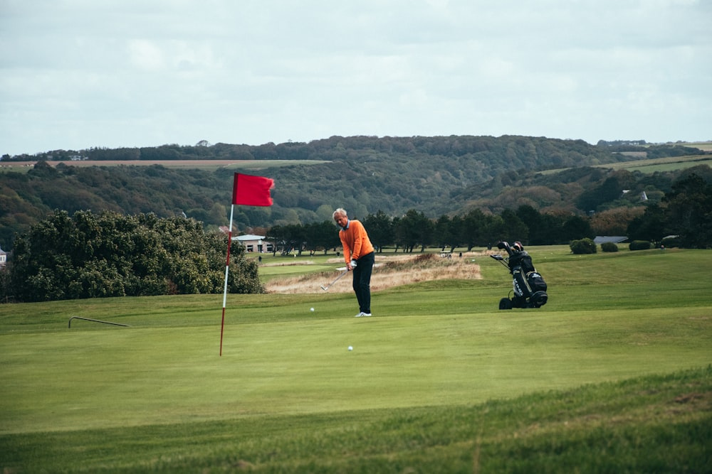 Hombre con chaqueta naranja y pantalones negros sosteniendo un palo de golf