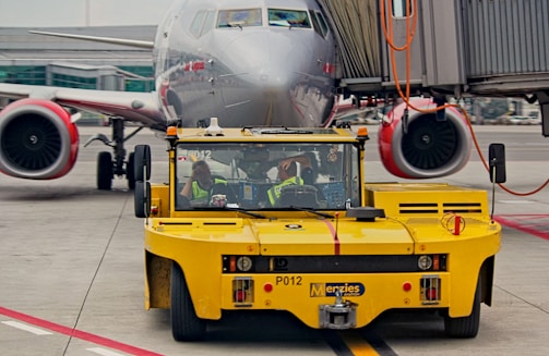 Technicians working on a sturdy aircraft towbar near a commercial jet.
