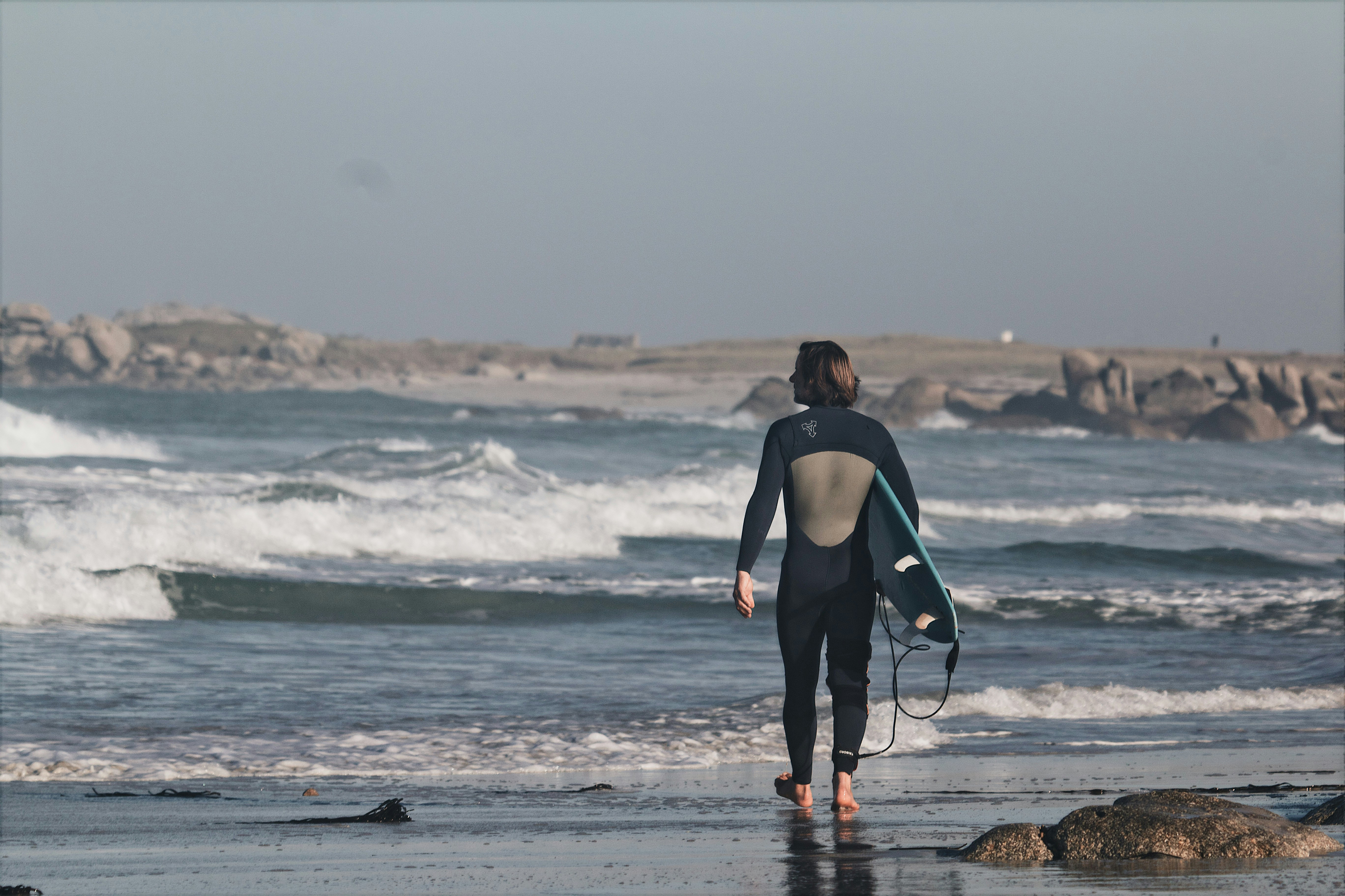 woman in black tank top holding black and white surfboard standing on seashore during daytime