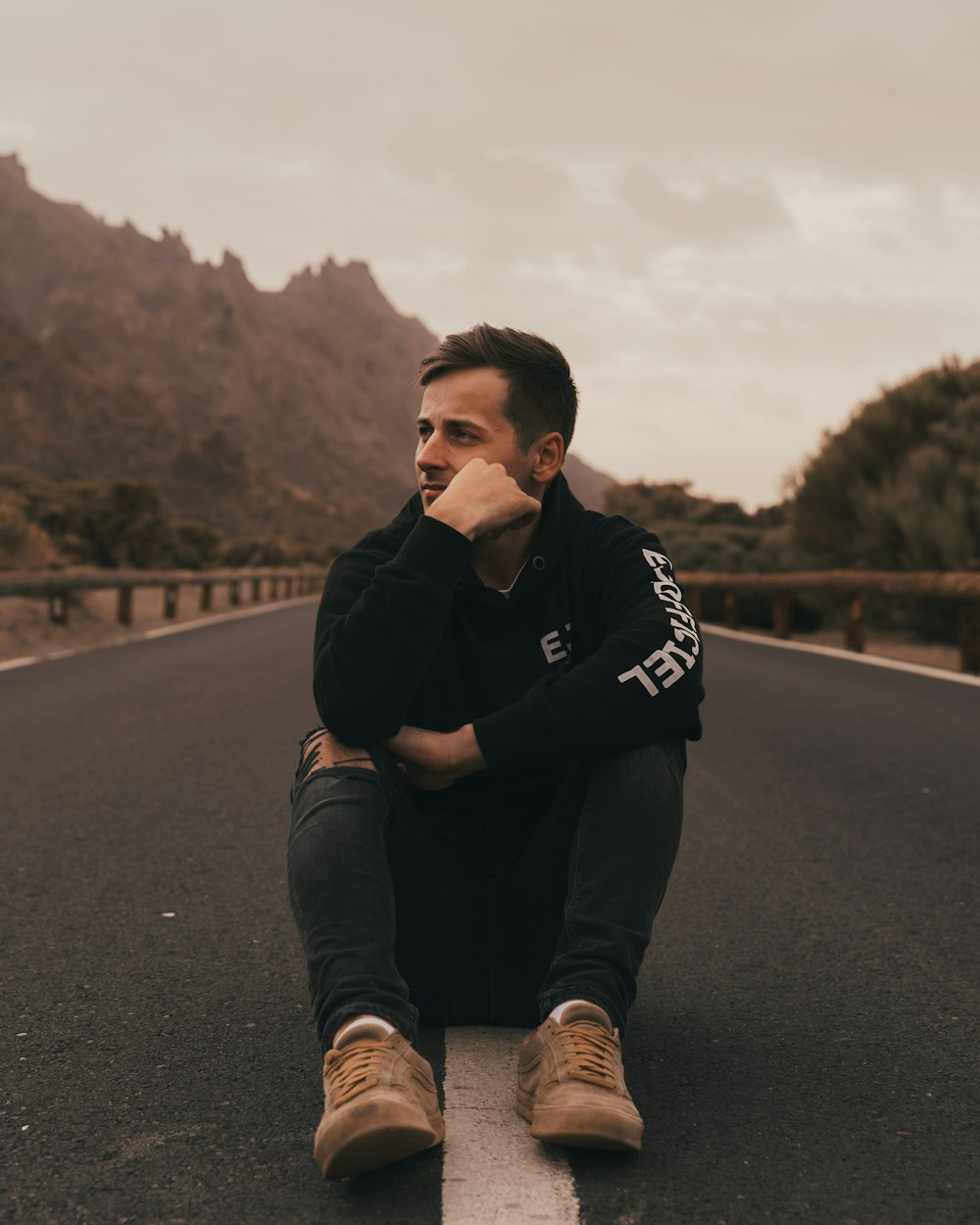 man in black and white hoodie sitting on the road during daytime