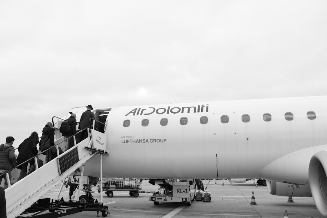 grayscale photo of man in black jacket and pants standing near white airplane,