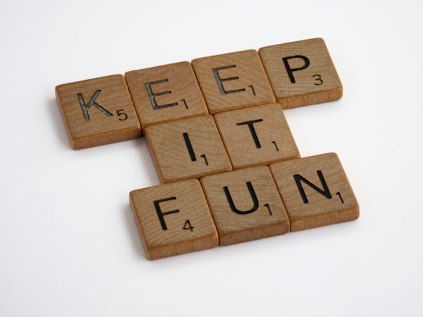 Wooden Scrabble tiles spell out the phrase 'KEEP IT FUN' against a plain white background. Each tile has a letter with a corresponding point value at the bottom right.