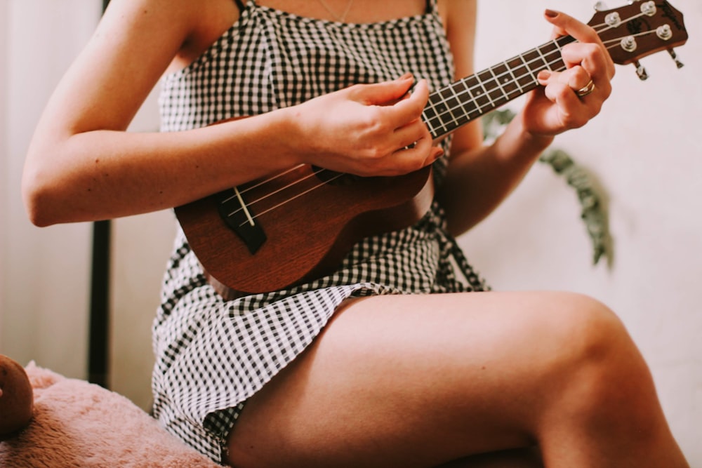 Frau in schwarz-weiß kariertem ärmellosem Kleid spielt braune akustische Gitarre