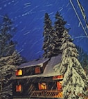 Night view of a chalet lit warmly from inside, snow gently falling outside.