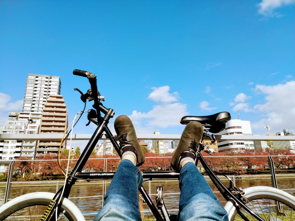 person in blue denim jeans and brown boots sitting on black bicycle during daytime