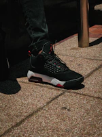 A close-up of a sleek black sneaker with bold red accents on a city sidewalk.
