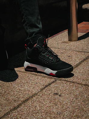A close-up of a sleek black sneaker with bold red accents on a city sidewalk.