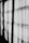 Black and white curtains hang in a row with light filtering through them, casting shadows and creating a pattern of lines and shapes on the fabric.