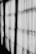 Black and white curtains hang in a row with light filtering through them, casting shadows and creating a pattern of lines and shapes on the fabric.