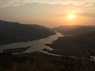 A serene sunset shot captured by drone over lush green hills and a winding river.