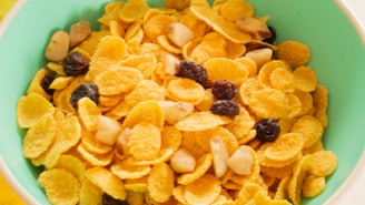 A green bowl filled with cornflakes mixed with raisins and nuts, creating a colorful and appetizing breakfast scene.
