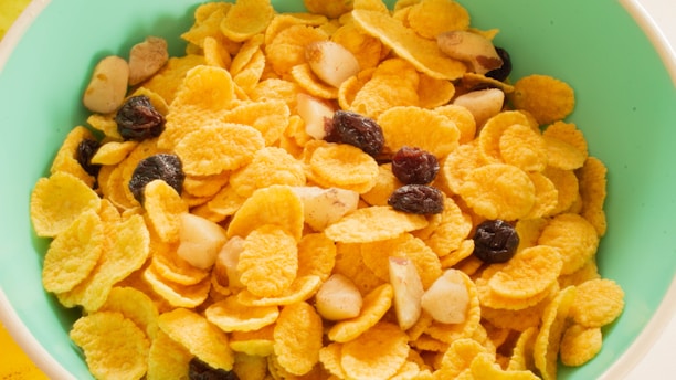 A green bowl filled with cornflakes mixed with raisins and nuts, creating a colorful and appetizing breakfast scene.