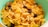 A close-up view of a bowl filled with cornflakes, mixed with nuts and raisins. The cornflakes are golden and crispy, while the nuts appear to be sliced, adding texture. The raisins are dark and scattered throughout, providing contrast.