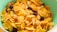 A close-up view of a bowl filled with cornflakes, mixed with nuts and raisins. The cornflakes are golden and crispy, while the nuts appear to be sliced, adding texture. The raisins are dark and scattered throughout, providing contrast.