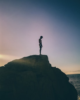 silhouette of man standing on rock formation during sunset