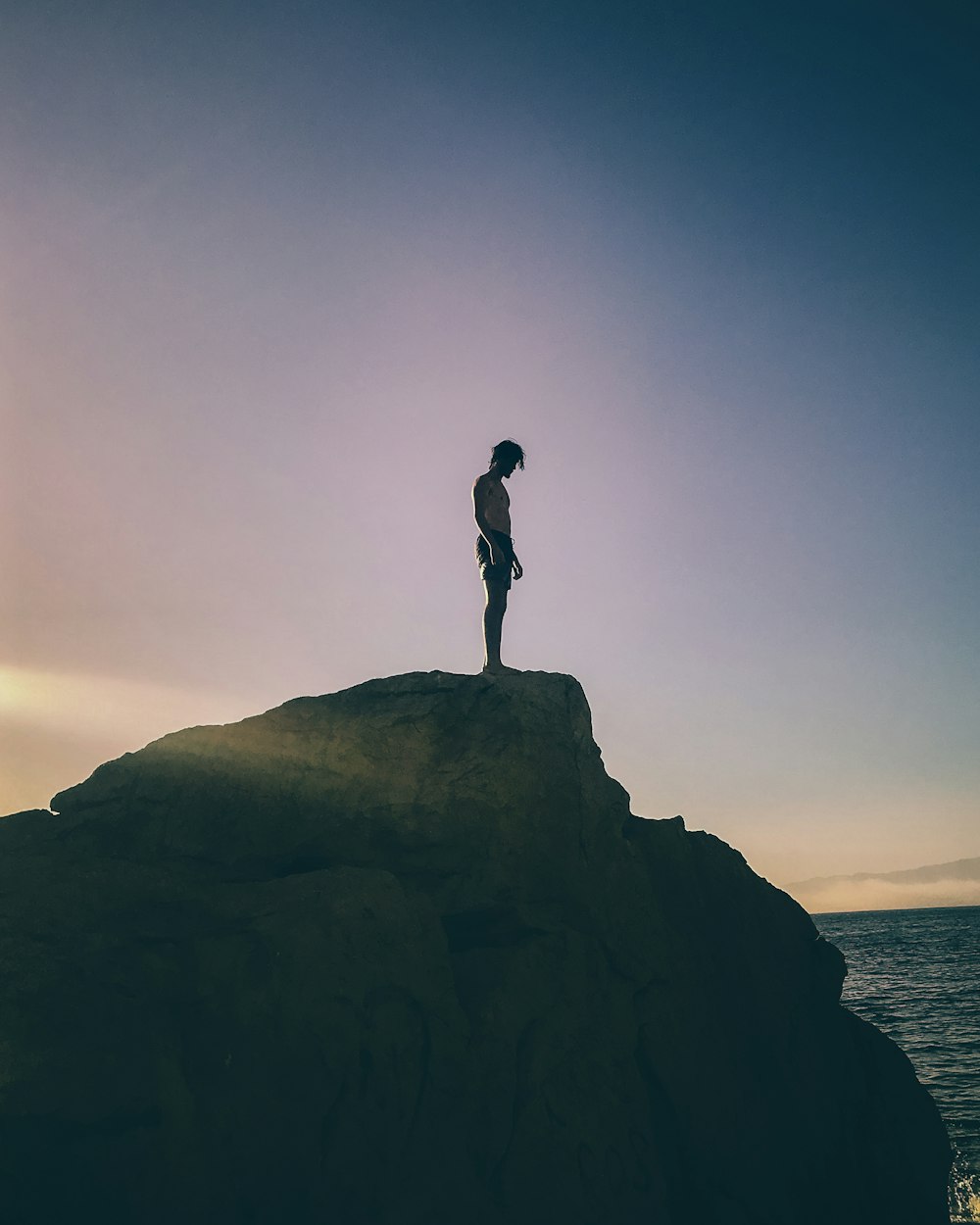 silhouette of man standing on rock formation during sunset