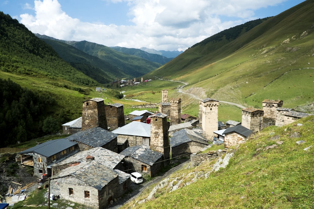 gray concrete houses on green grass field near green mountains under white clouds during daytime