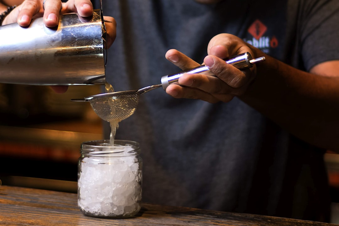 person pouring water on stainless steel cup, cocktails season 2019