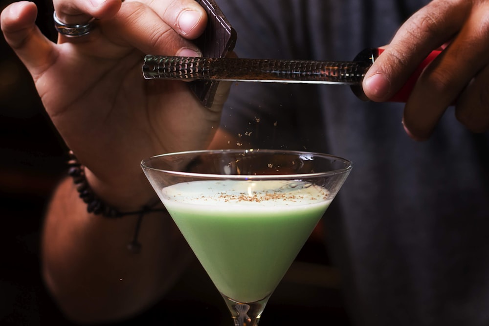 person holding clear drinking glass with green liquid