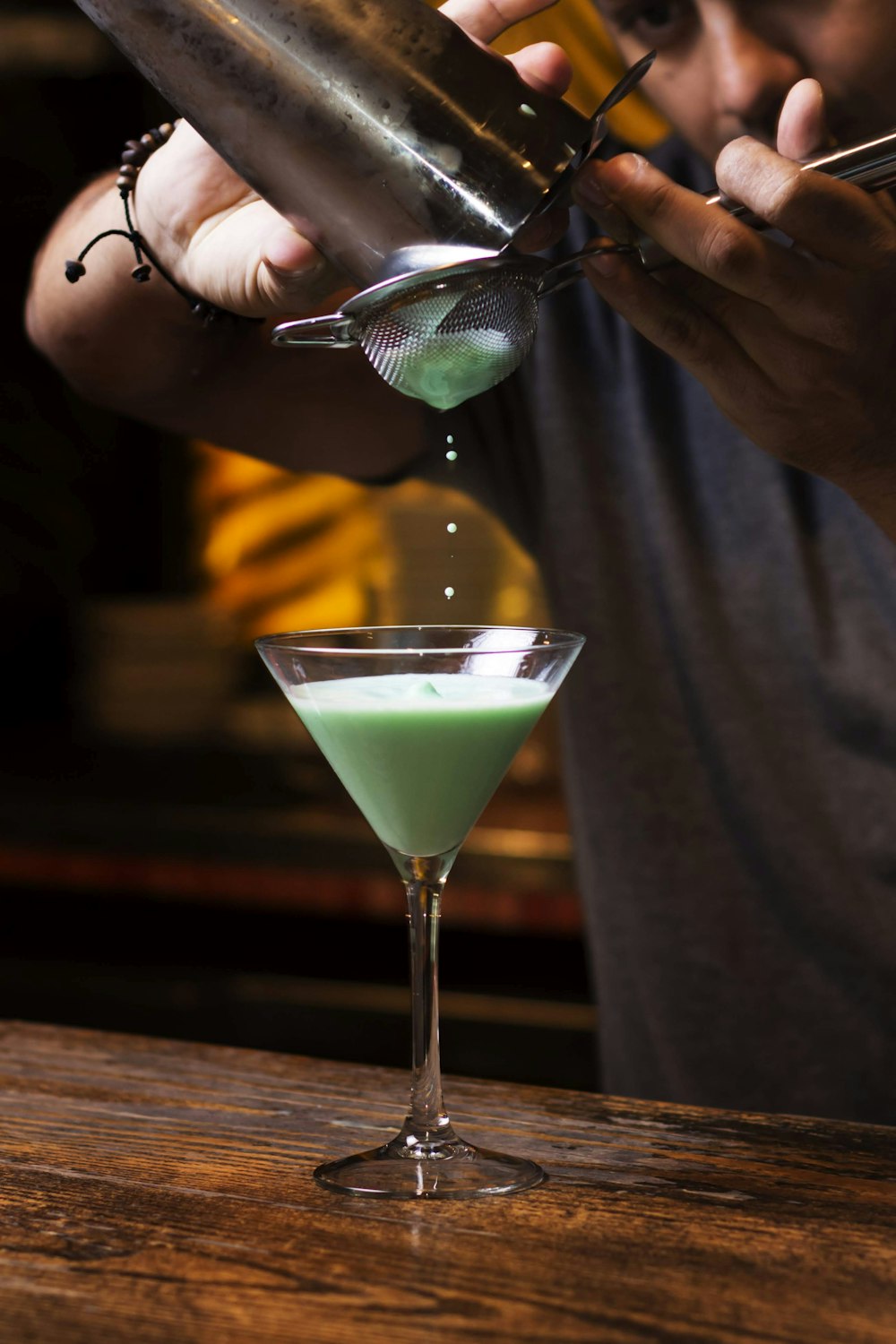person holding clear cocktail glass with green liquid