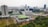 An aerial view of a large urban area featuring a mix of modern high-rise buildings and lower structures with distinctive green roofs, set against a backdrop of a sprawling cityscape. The lush greenery and landscaped gardens are visible in the foreground, contrasting with the dense urban environment.