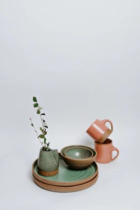 A bright collection of stoneware cups and vases arranged on a soft linen cloth with fresh flowers.