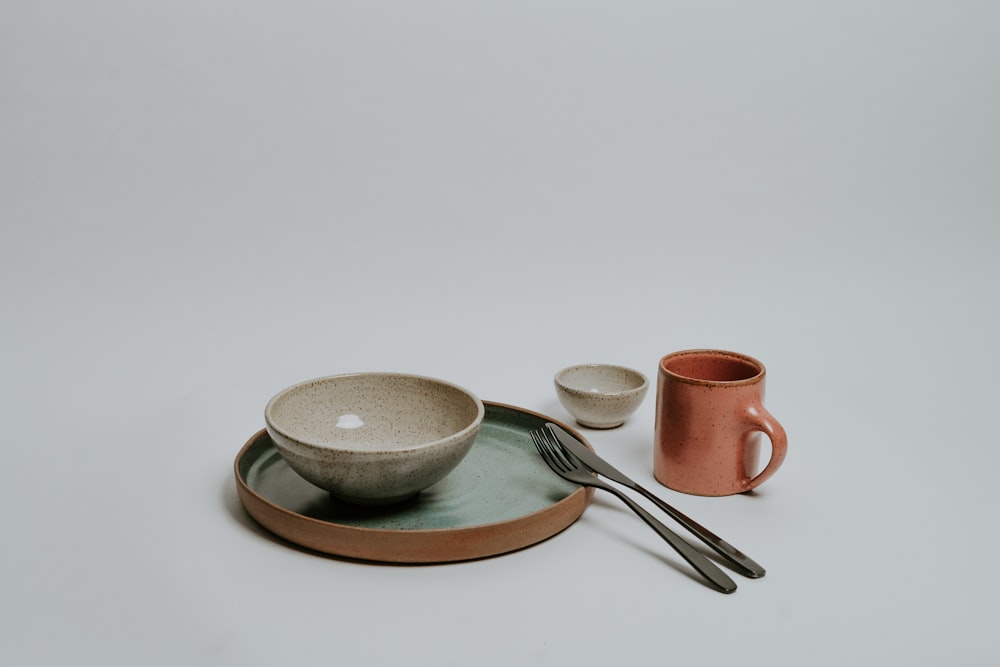 taza de té de cerámica blanca en platillo al lado de la cuchara y el tenedor de acero inoxidable