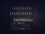 A dark toolset containing an array of metallic socket wrenches and attachments neatly arranged in a hard case. The tools have a reflective surface, and the case has defined slots for each tool, creating an orderly appearance.