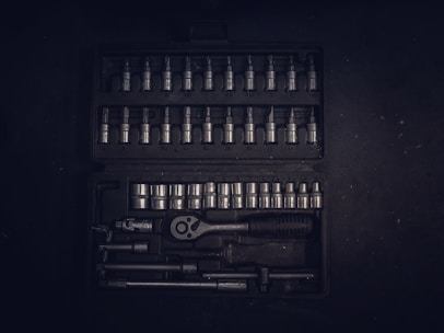 A dark toolset containing an array of metallic socket wrenches and attachments neatly arranged in a hard case. The tools have a reflective surface, and the case has defined slots for each tool, creating an orderly appearance.