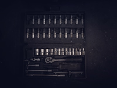 A dark toolset containing an array of metallic socket wrenches and attachments neatly arranged in a hard case. The tools have a reflective surface, and the case has defined slots for each tool, creating an orderly appearance.