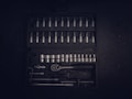 A dark toolset containing an array of metallic socket wrenches and attachments neatly arranged in a hard case. The tools have a reflective surface, and the case has defined slots for each tool, creating an orderly appearance.