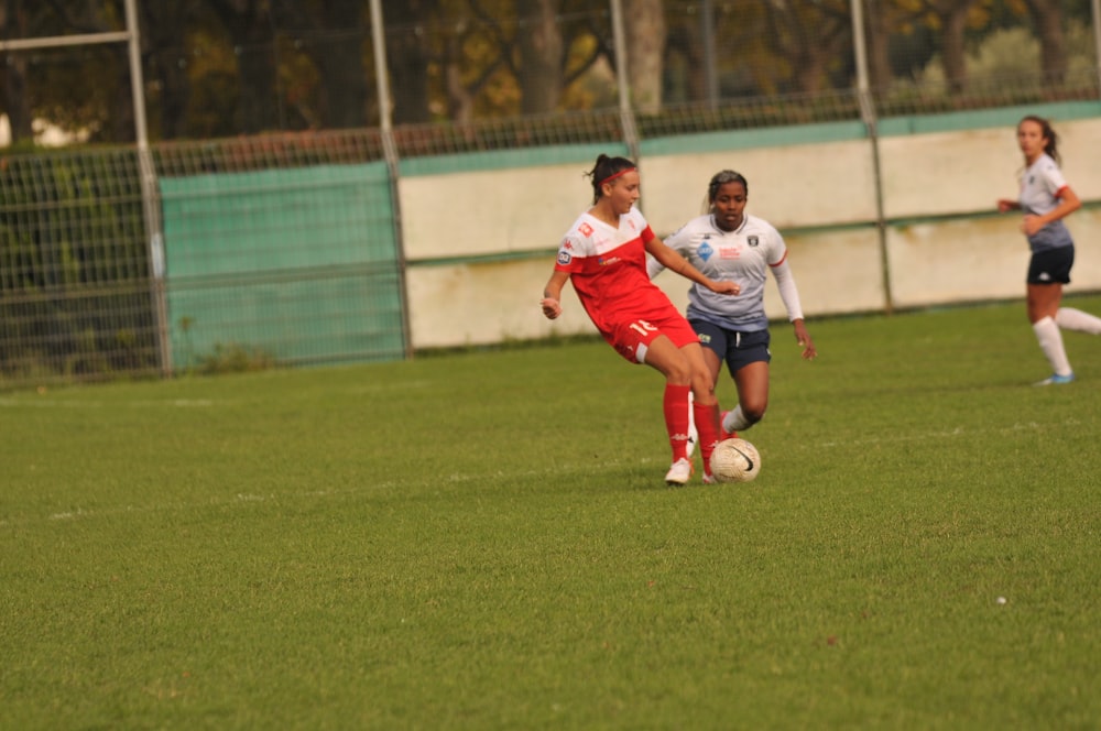 2 women in white and red soccer uniform playing on green grass field during daytime