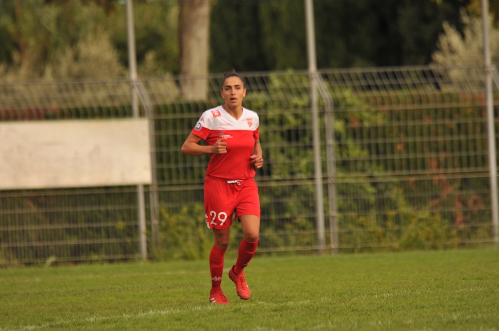 woman in red and white jersey shirt and red pants running on green grass field during