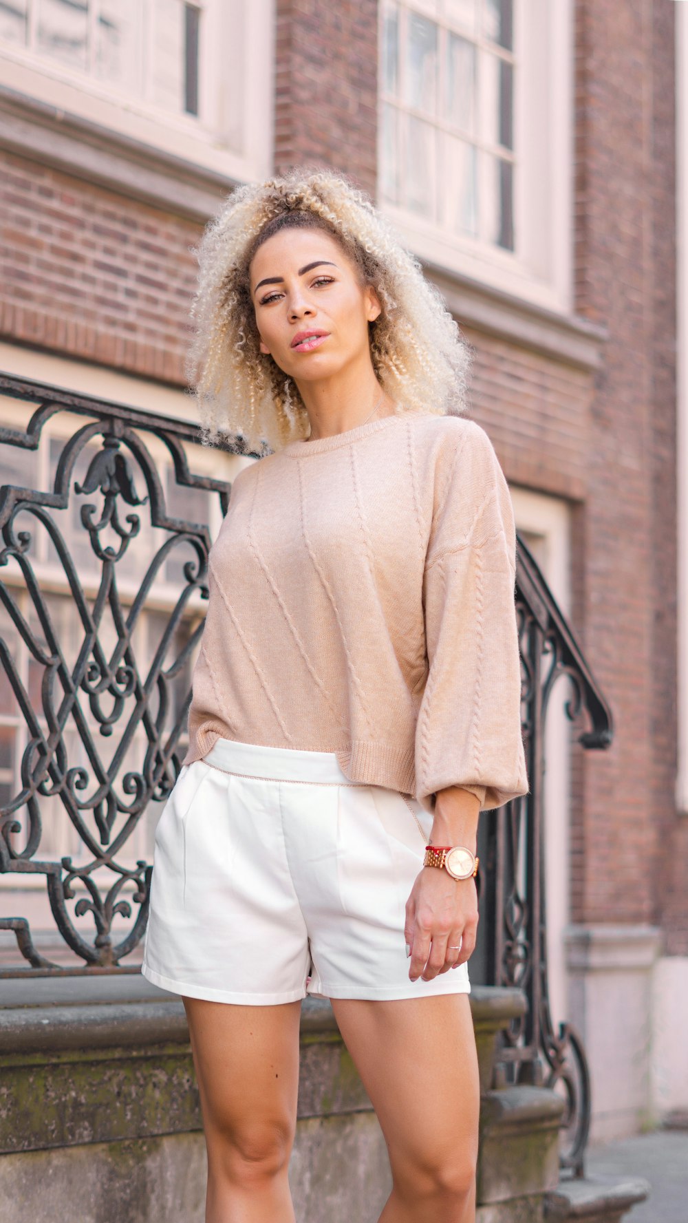 woman in beige long sleeve shirt and white skirt standing beside black metal fence during daytime