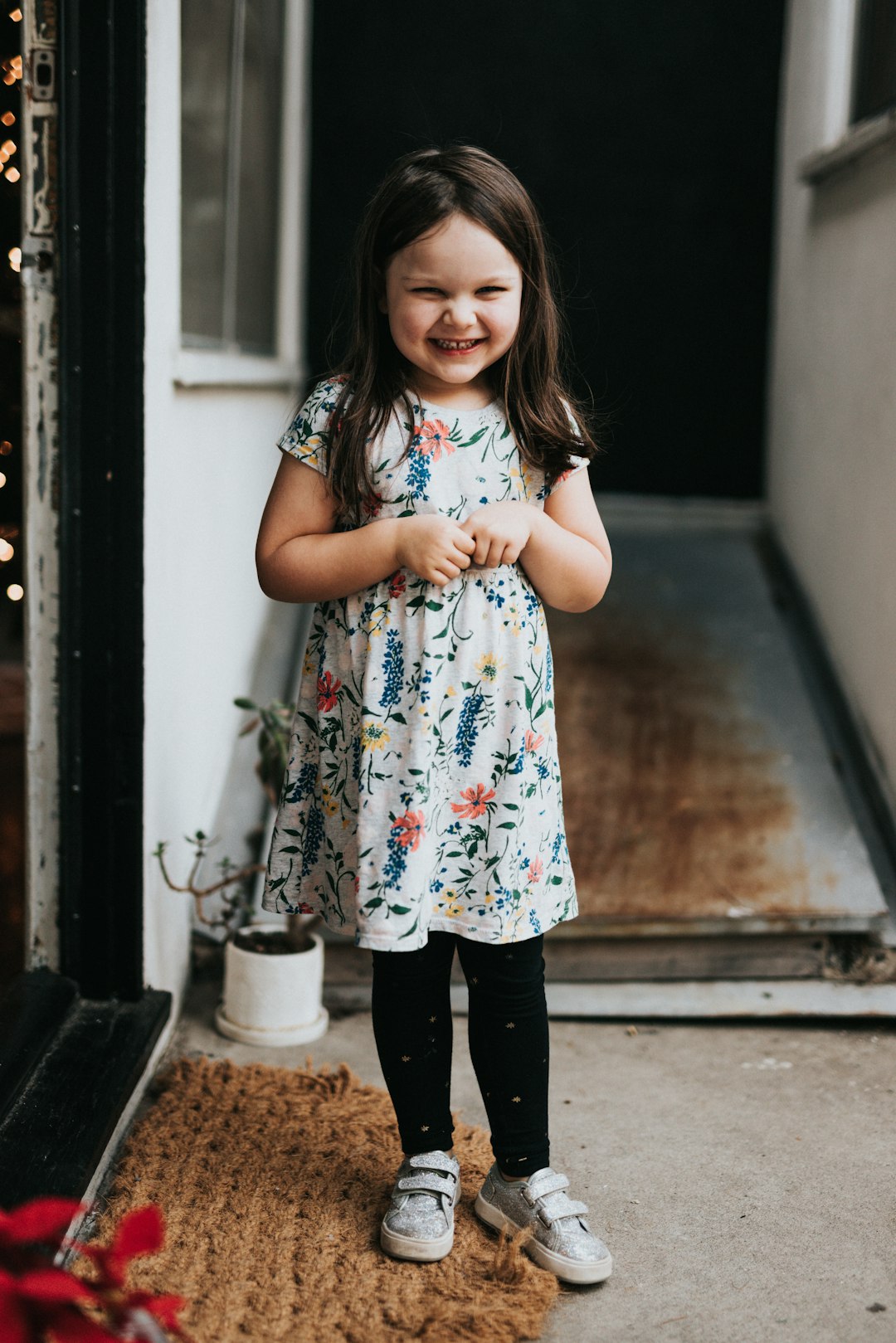 girl in white red and green floral dress standing on gray concrete floor