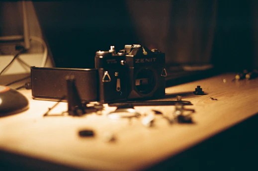 A close-up of a mechanical engineer's hands assembling a vintage camera, surrounded by tools and blueprints.