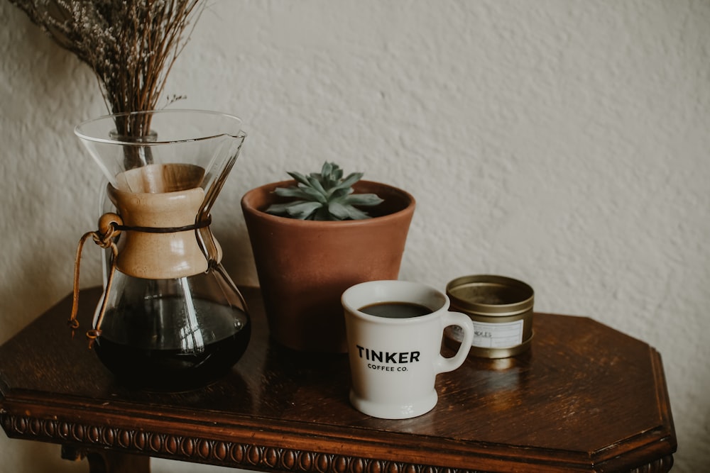 a wooden table topped with a cup of coffee next to a potted plant