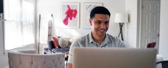 man in gray hoodie sitting on chair in front of silver macbook