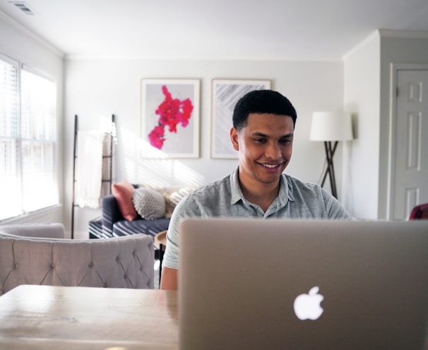 man in gray hoodie sitting on chair in front of silver macbook