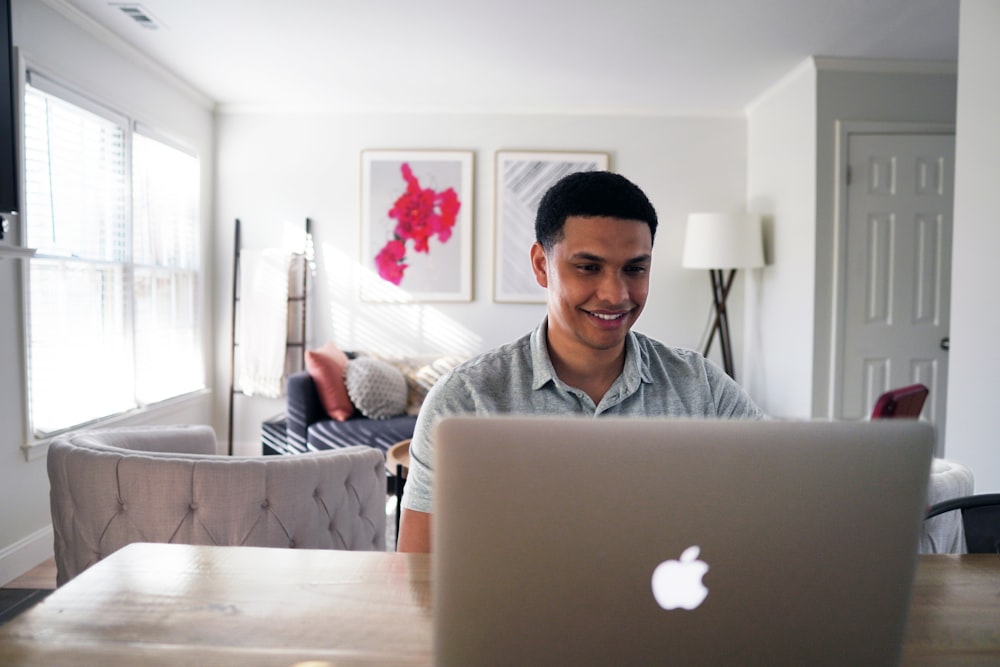 シルバーのMacBookの前の椅子に座っているグレーのパーカーを着た男