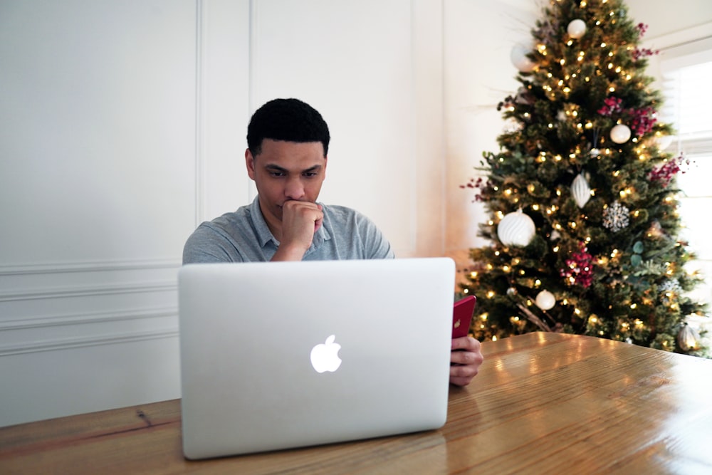 Mann im grauen Rundhalshemd sitzt vor dem silbernen MacBook