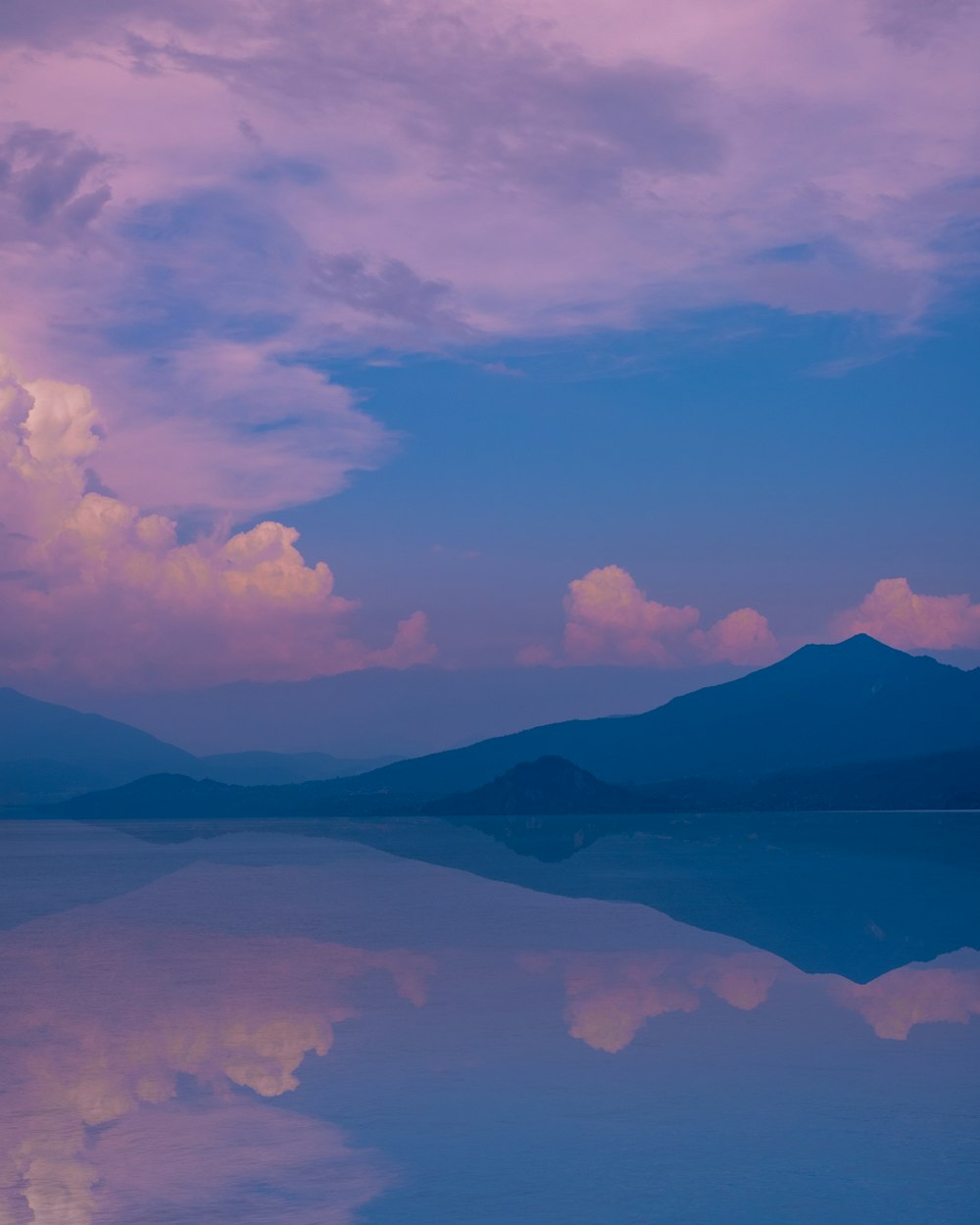 body of water near mountain under white clouds and blue sky during daytime