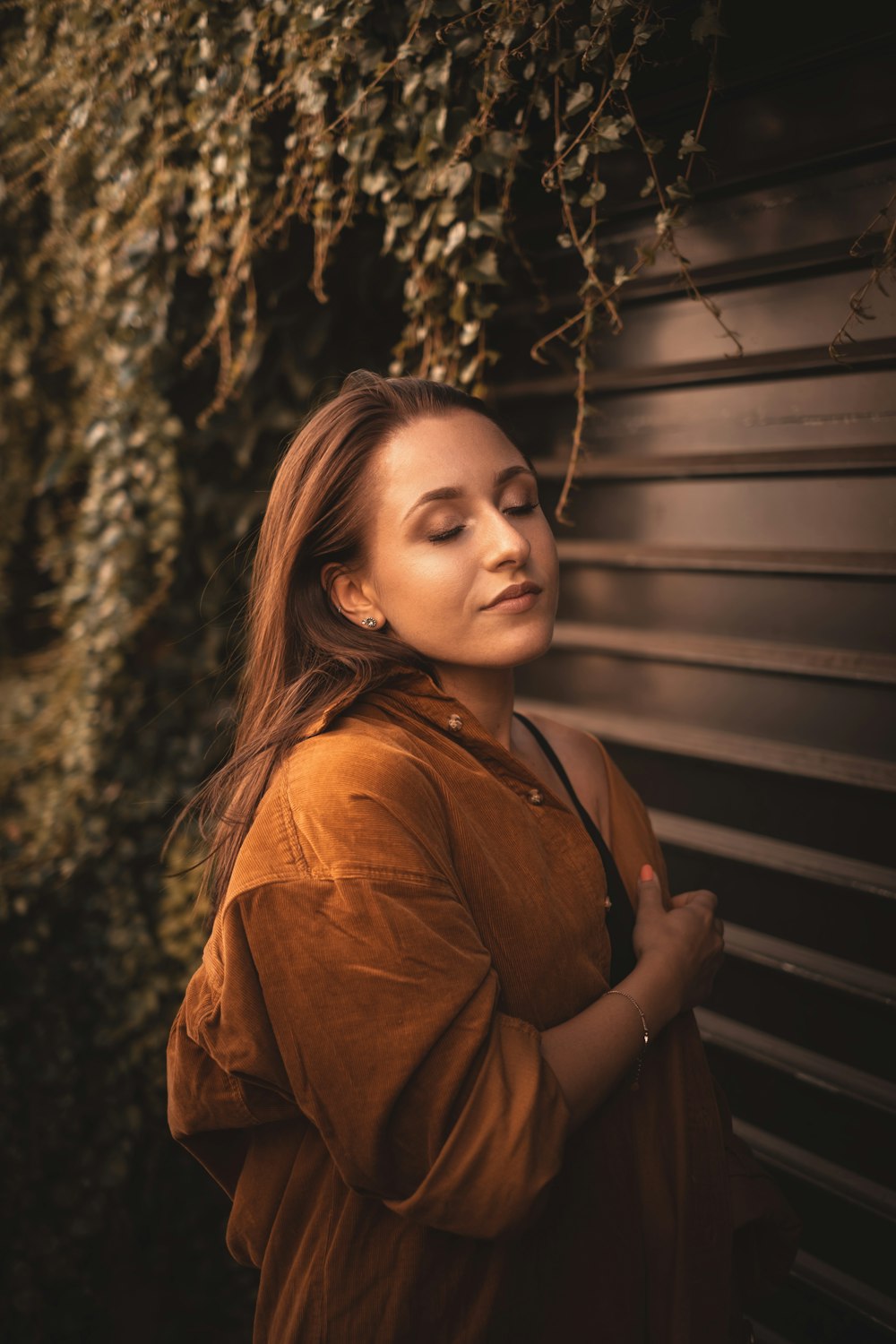 woman in brown leather jacket standing beside green wooden wall