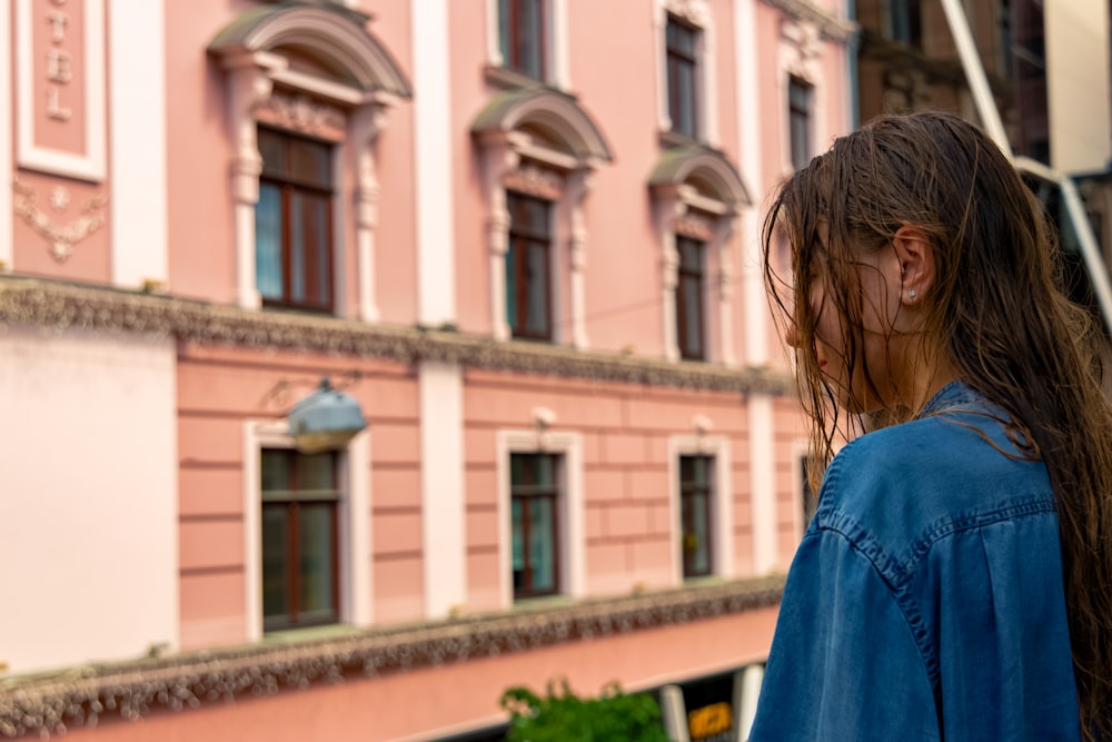 Mujer con camisa azul de pie cerca de un edificio de hormigón marrón durante el día