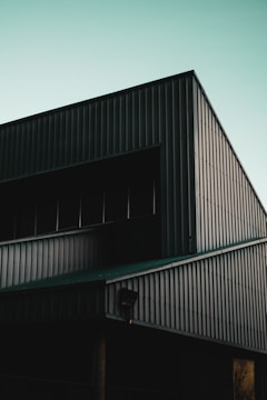 A portion of a modern industrial building with a slanted roof and corrugated metal siding, under a clear sky with a hint of sunset light.